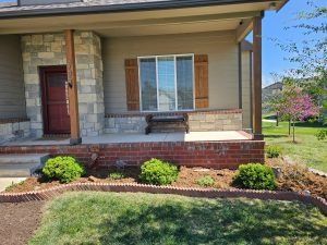 A house front porch with brick and stone accents. Green bushes line the yard.