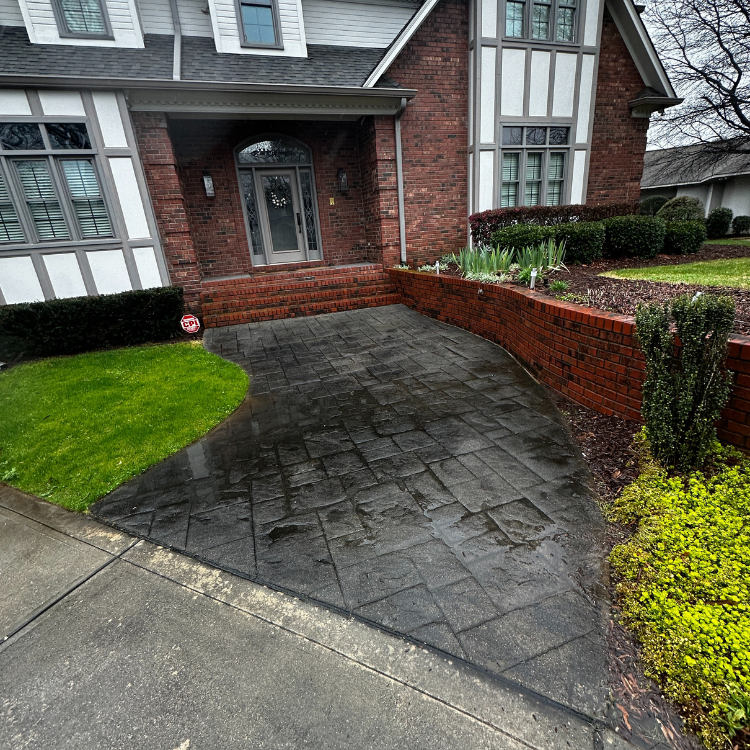 Brick home with stamped concrete driveway; green lawn, brick wall, and shrubs.