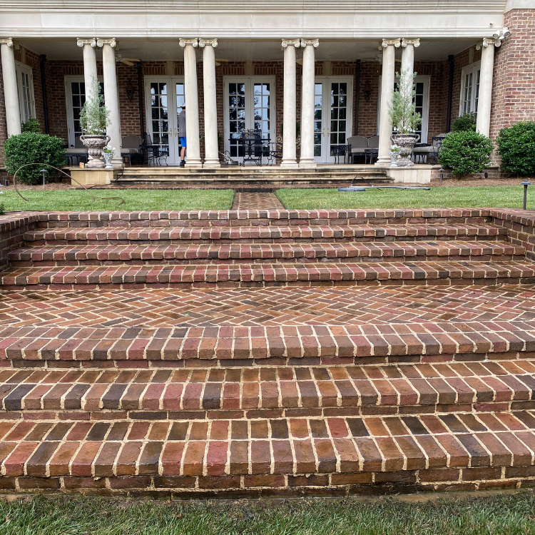 Brick steps leading up to a home with columns and double doors. Green lawn in foreground.