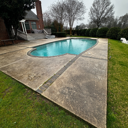 Concrete pool with turquoise water in a backyard, cloudy sky overhead.