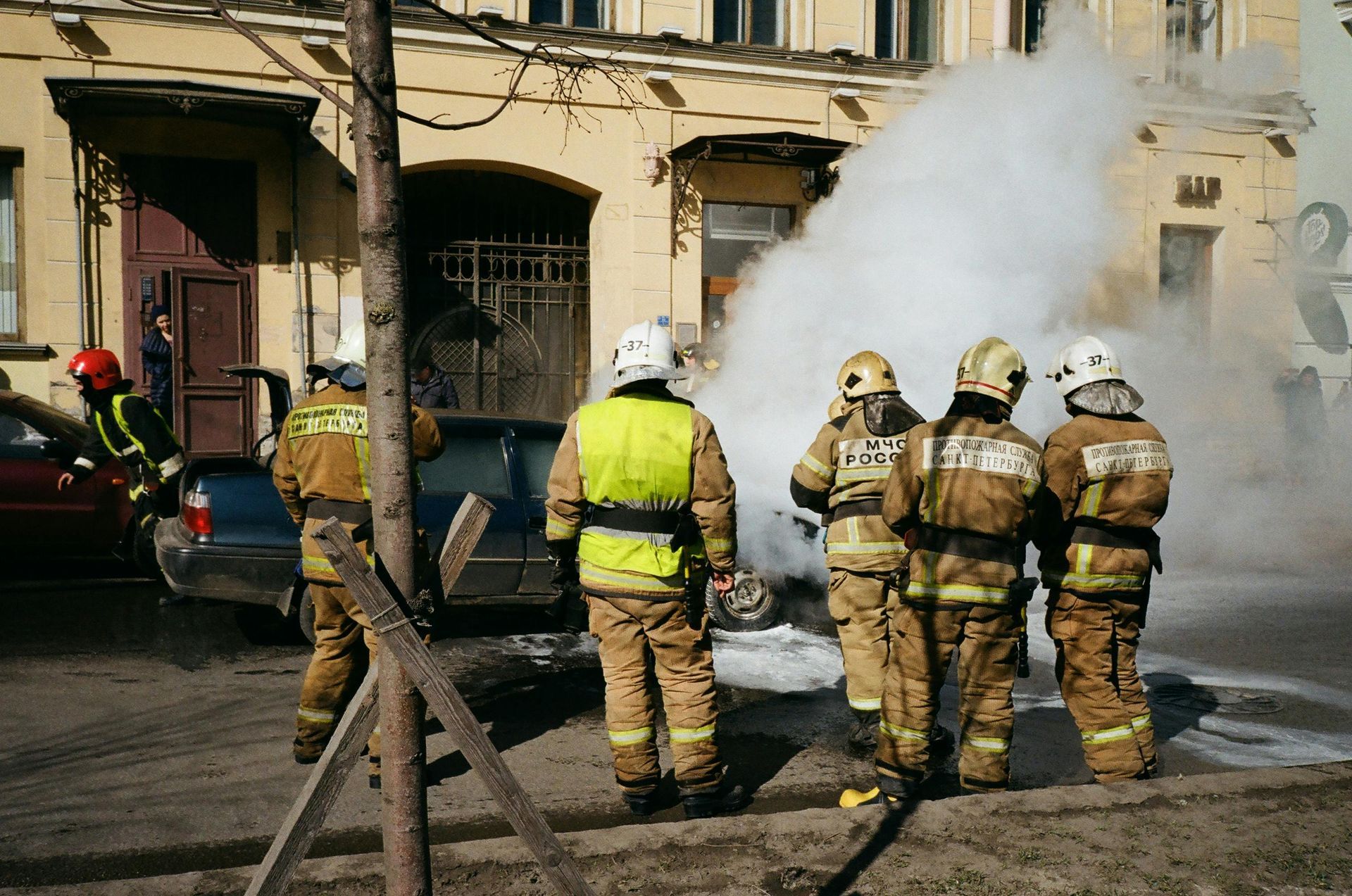 A group of firefighters are standing in front of a building with smoke coming out of it.