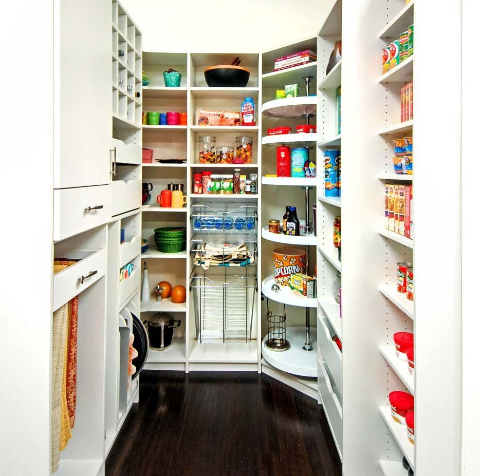 A well-organized pantry with white shelves, a corner rotating rack, drawers, and various food items on dark floors.