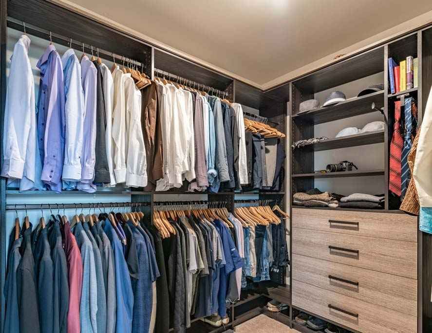 Walk-in closet with organized clothing hanging on racks and a wooden dresser unit with shelving.