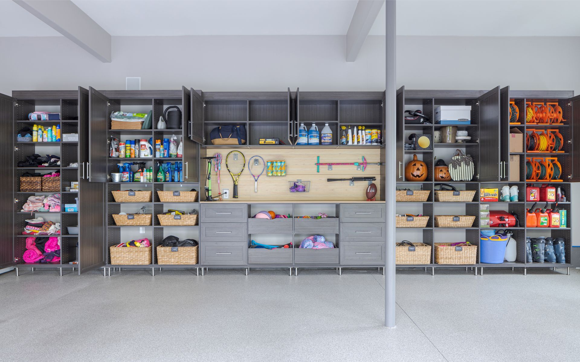 Large dark gray garage storage system with open shelves, cabinets, and woven baskets filled with organized belongings.