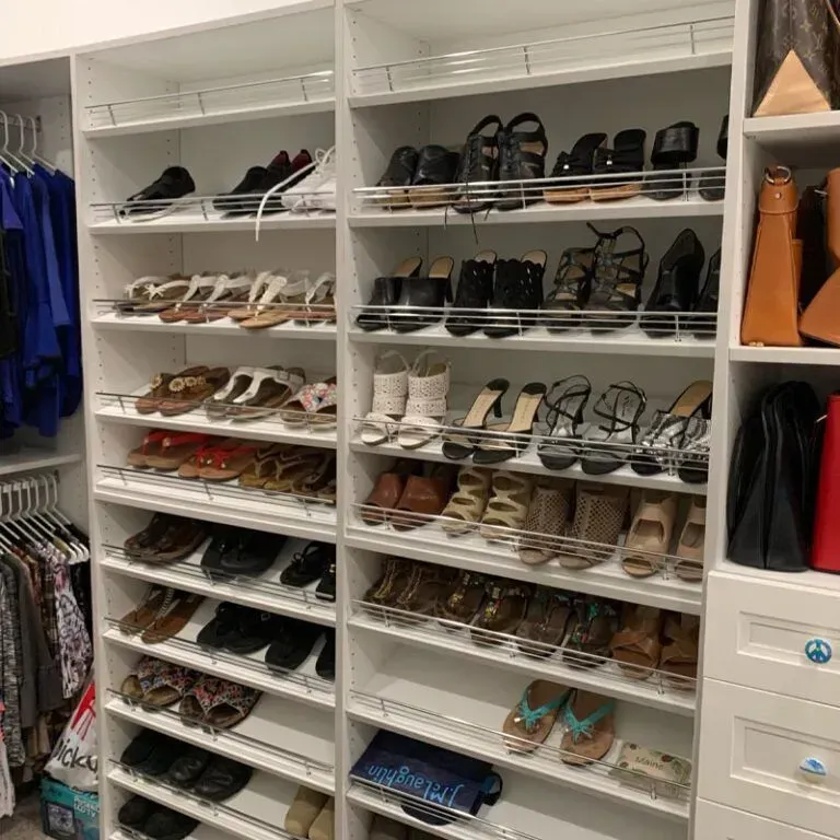 A walk-in closet with organized white shelves holding numerous pairs of women's shoes and handbags.