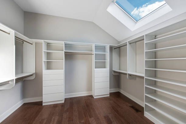 A walk-in closet with white shelving, multiple drawers, hanging rods, and hardwood floors under a sloped skylight.