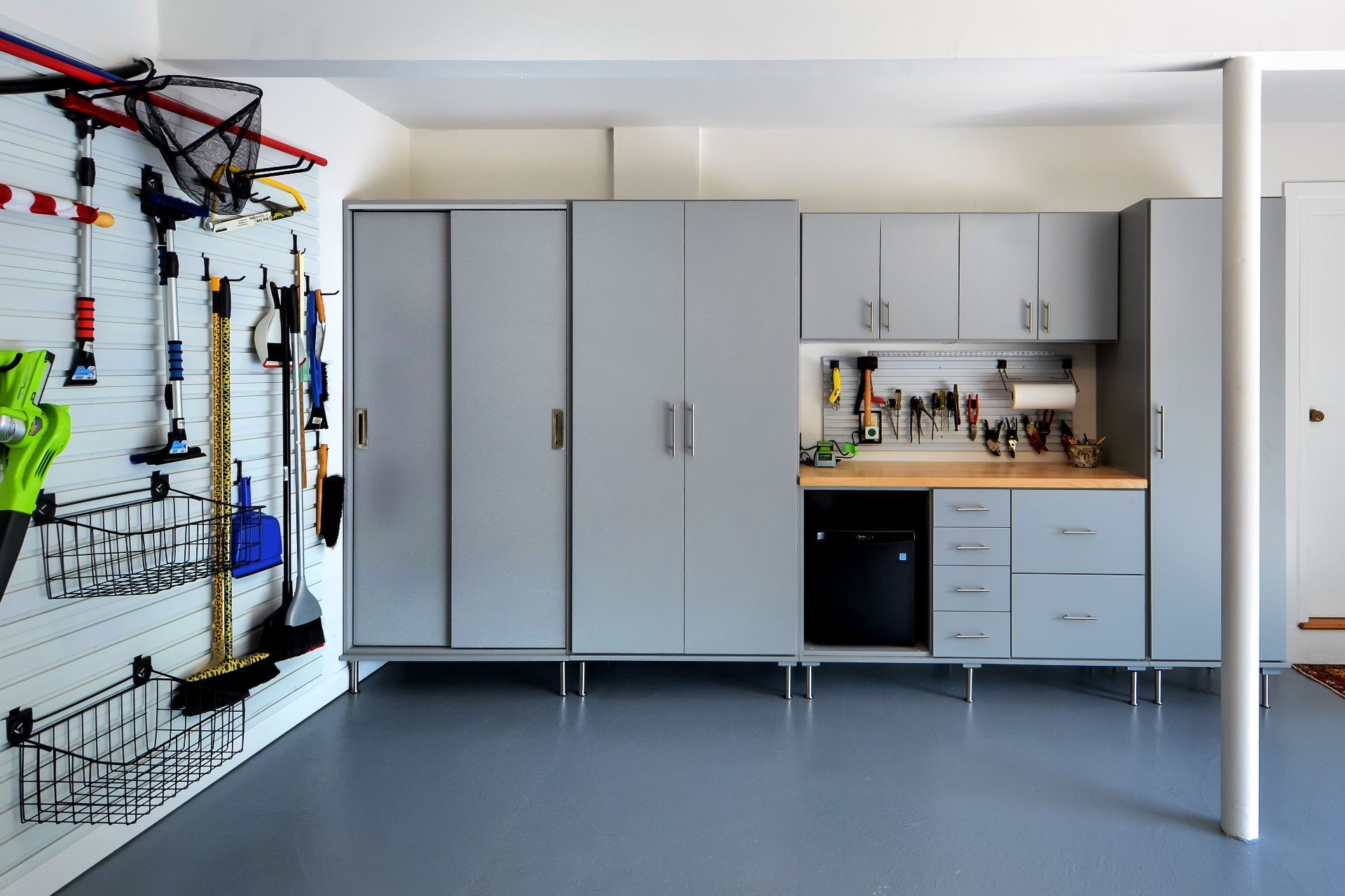 Organized white pantry shelving with various shelves, pull-out drawers, wire baskets, and hanging kitchen linens.