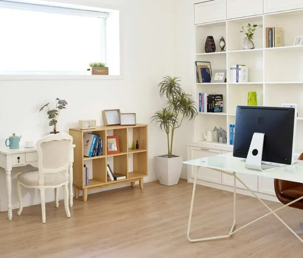 A bright, modern home office with a white desk, chair, wooden shelving, and a large computer workspace.