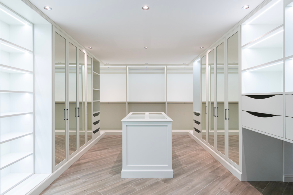 A modern, symmetrical walk-in closet featuring white cabinetry, glass-front wardrobe doors, LED lighting, and wood floors.