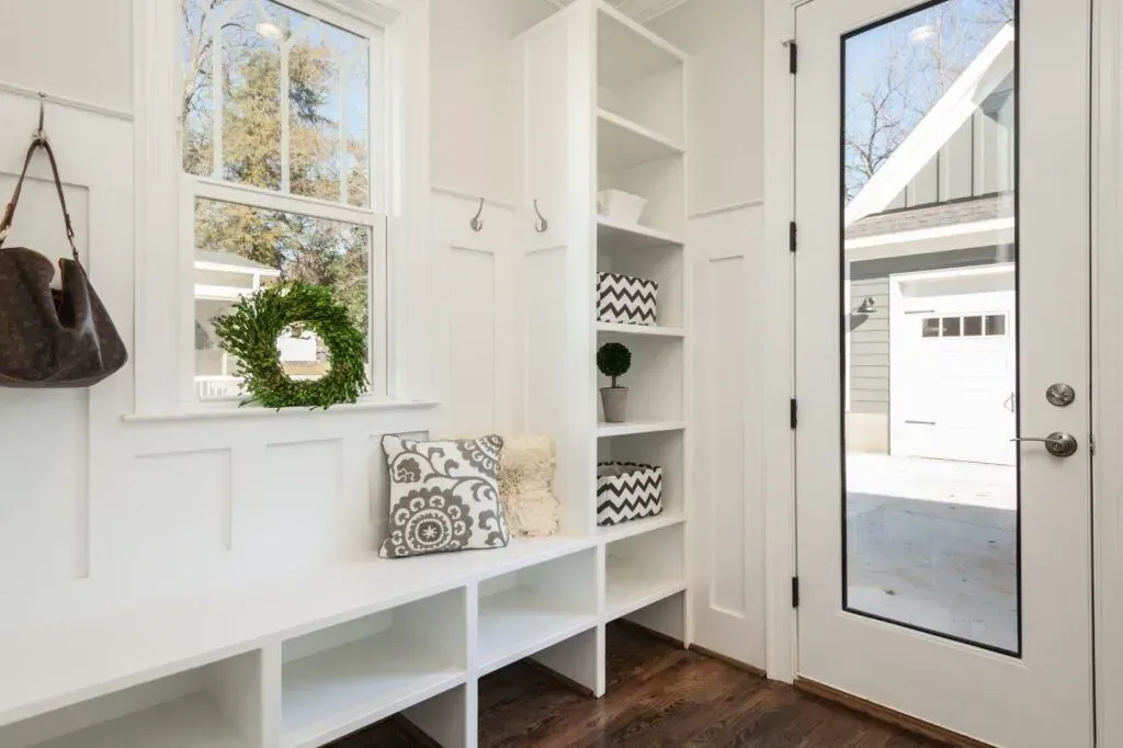 White mudroom entryway with a bench, open storage shelves, a window, coat hooks, and a glass-paneled door.