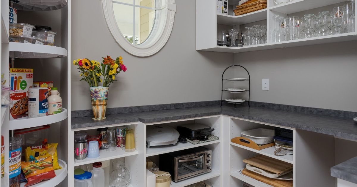 A well-organized pantry featuring white shelving, grey countertops, a small oval window, and various kitchen items.
