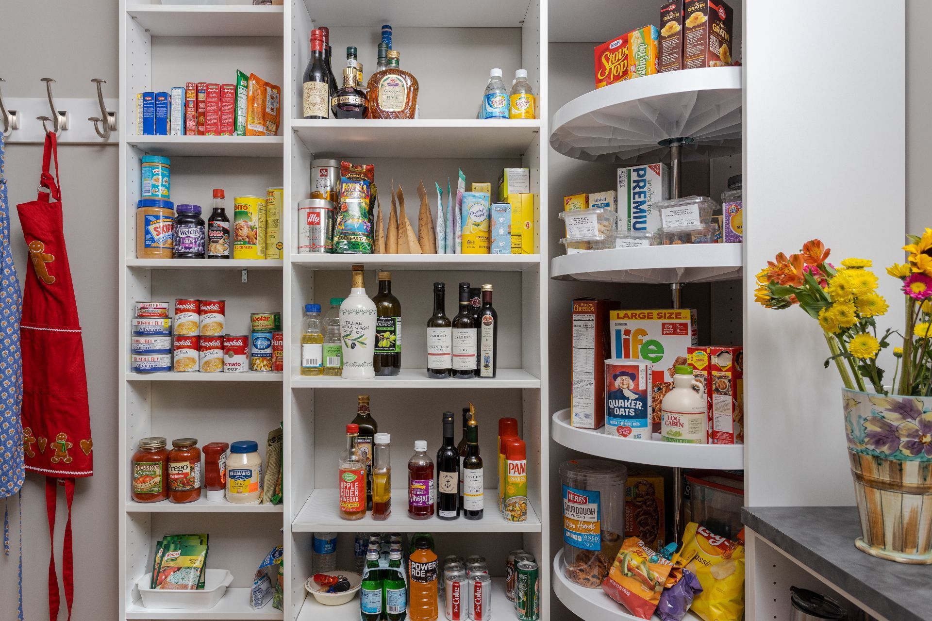 A well-organized white pantry with shelves stocked with food items, bottles, and a rotating corner storage unit.