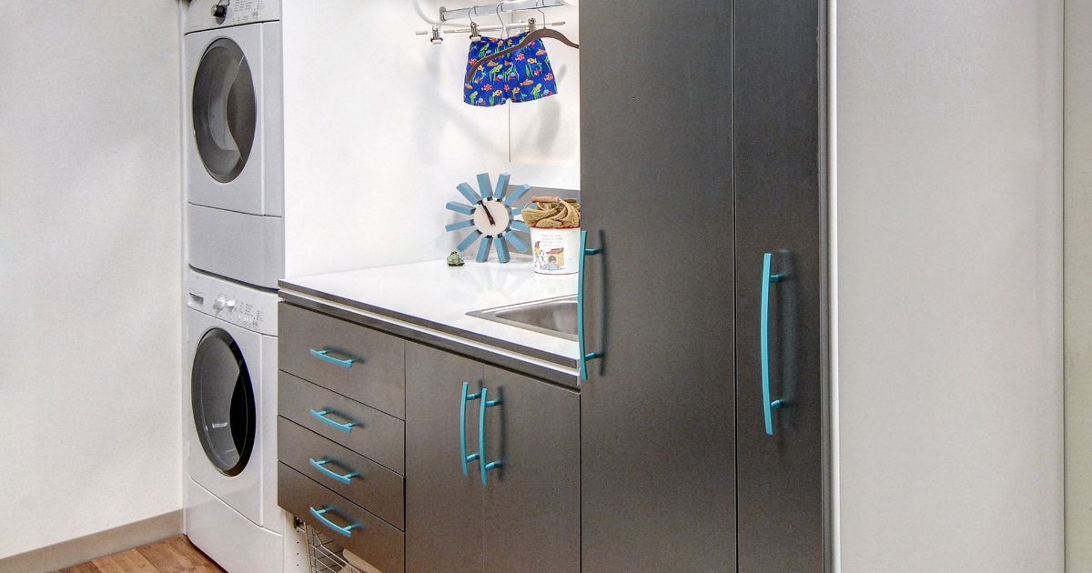 A laundry room featuring a stacked washer and dryer next to dark grey cabinets with bright blue handles and a countertop.