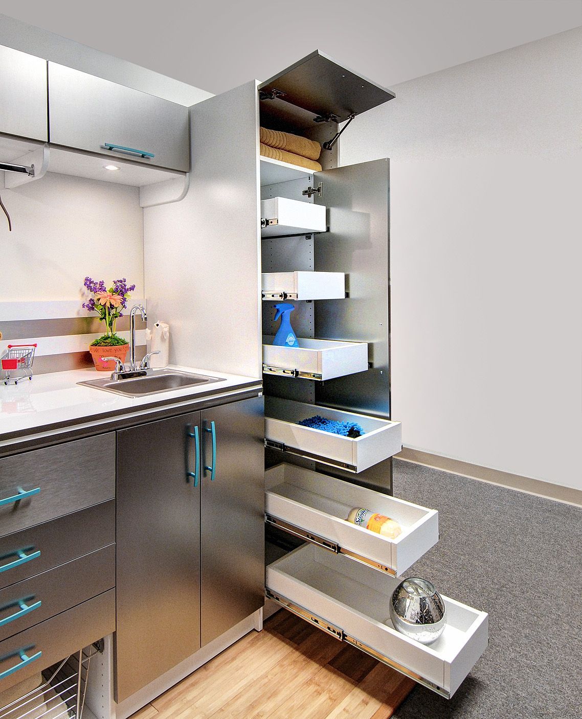 Stainless steel cabinet unit with a tall, open pantry containing multiple pull-out drawers, beside a kitchen sink area.