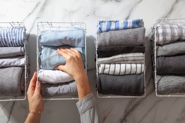 Hands organize folded clothes into wire baskets arranged on a marble surface.