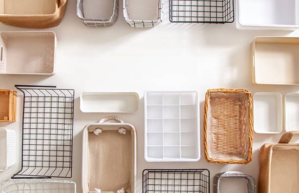 A top-down view of various empty storage bins, baskets, and drawer organizers in neutral tones arranged on a white surface.