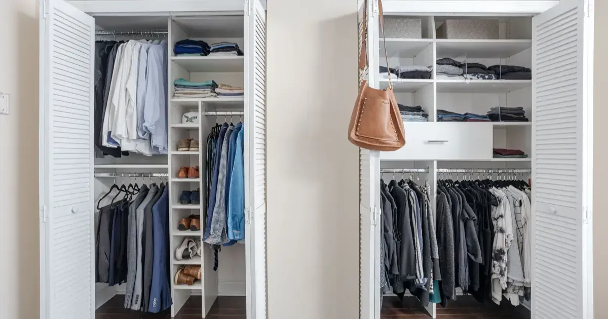 Two open white louvered closets filled with neatly organized hanging clothes, shelves, and a tan handbag hanging inside.