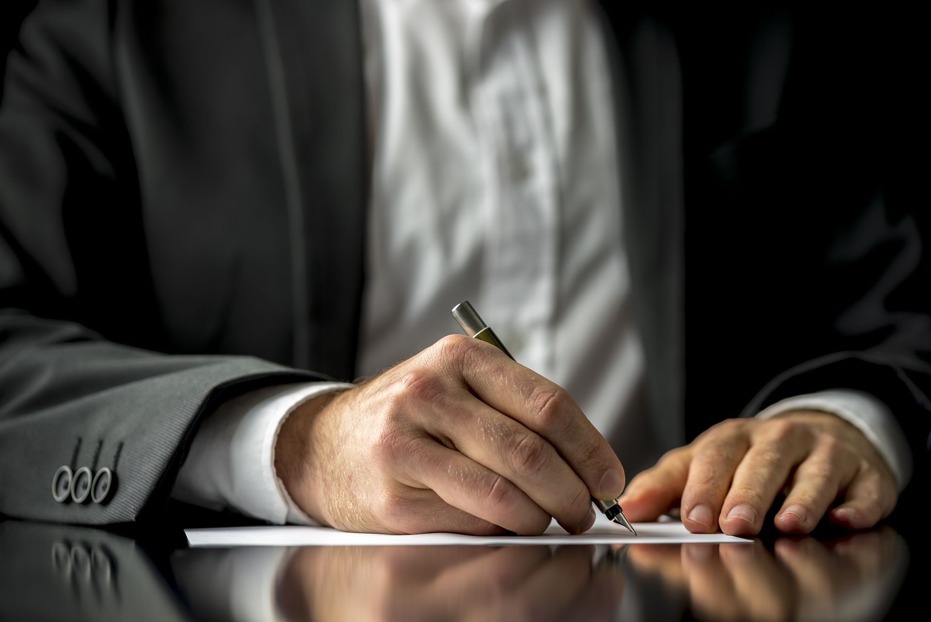 A man in a suit is writing on a piece of paper with a pen
