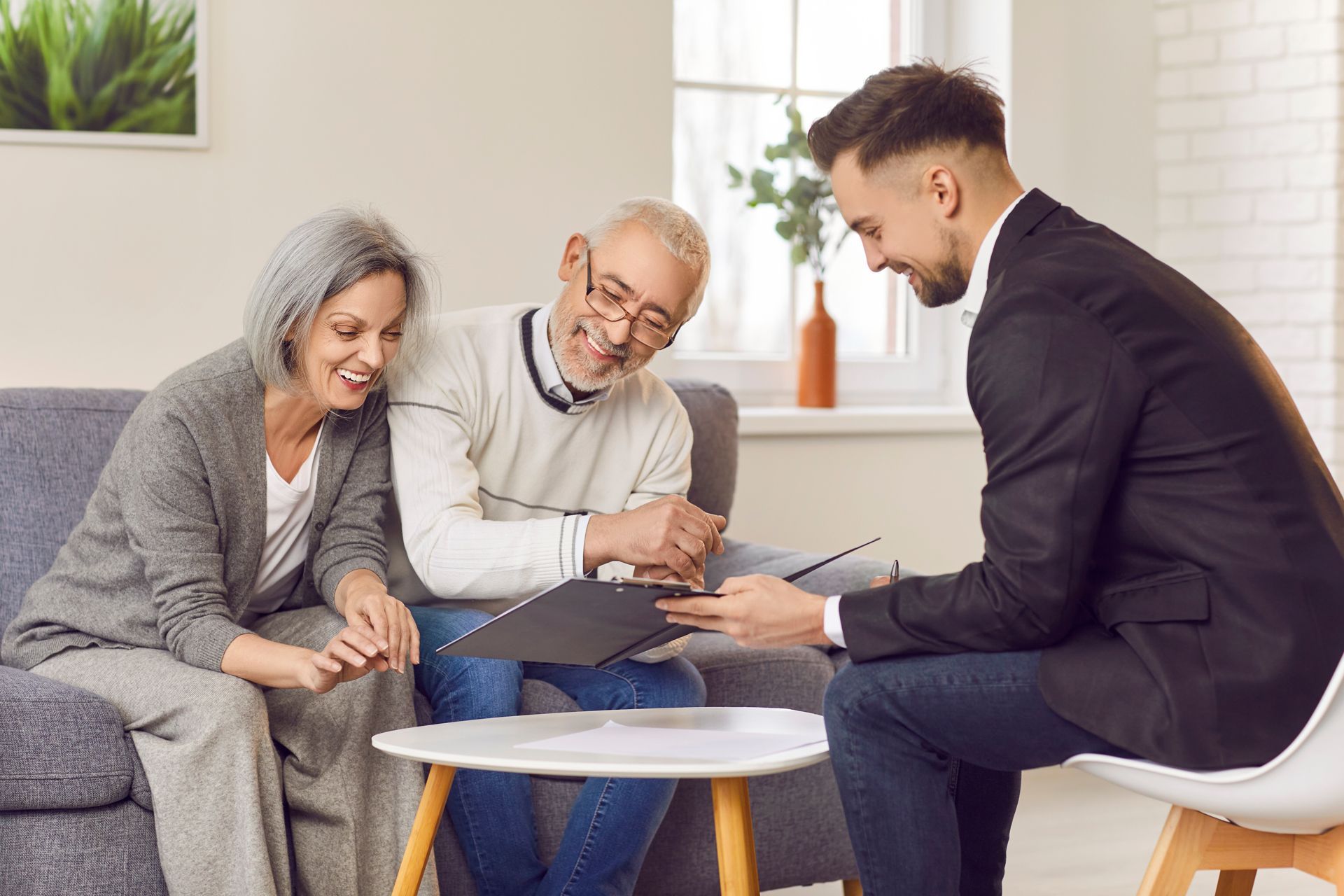 An elderly couple is sitting on a couch talking to a man in a suit