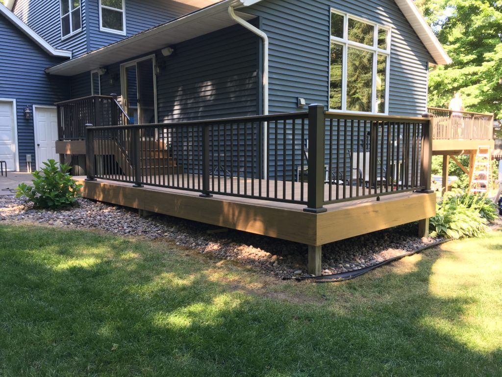 A wooden deck with a black railing is in front of a blue house.