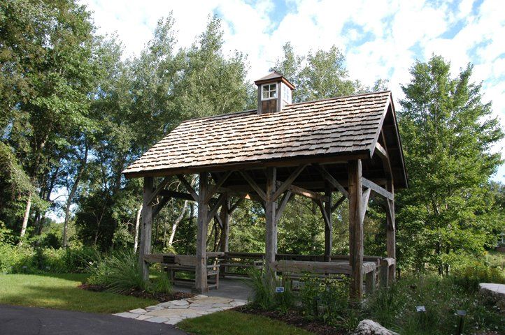 A wooden gazebo with a roof in the middle of a backyard