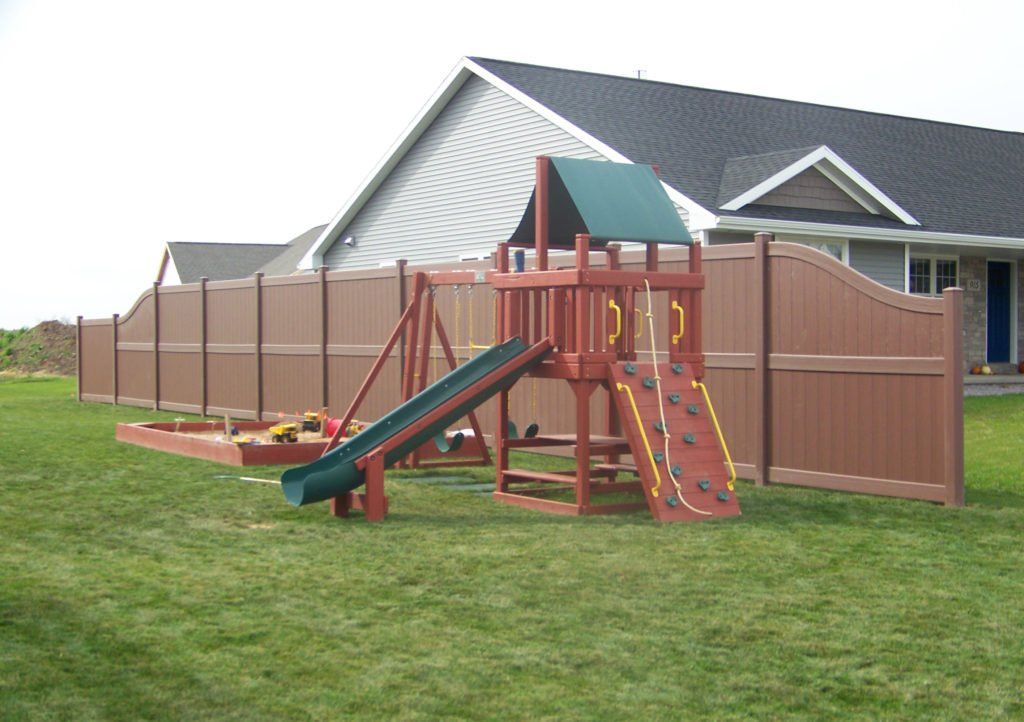 A playground with a slide and a brown vinyl fence