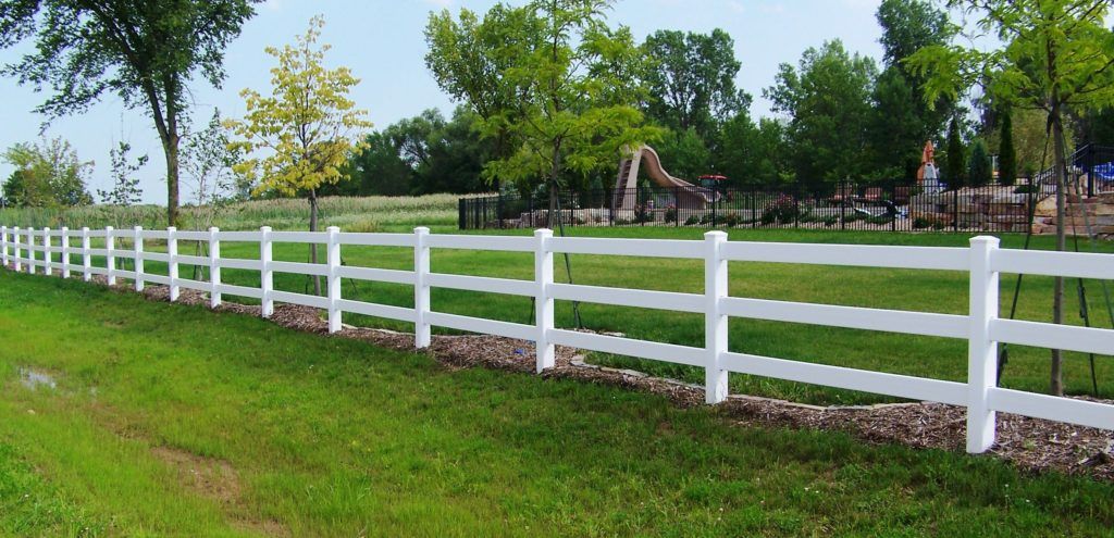 A white fence surrounds a grassy field with trees in the background.
