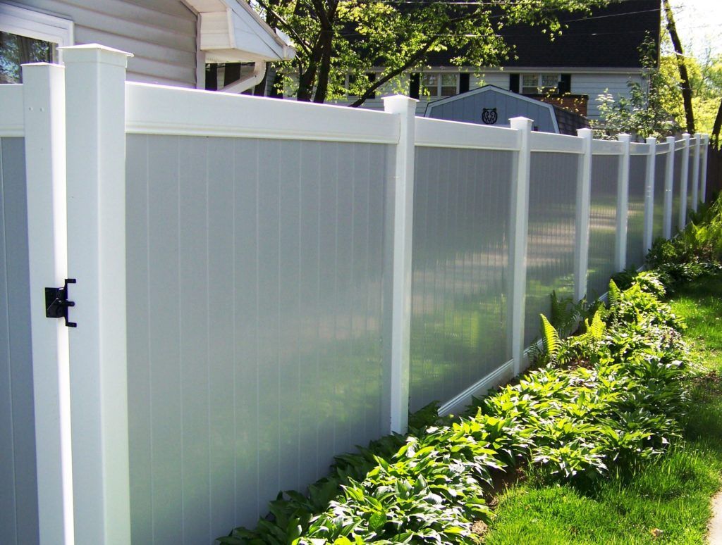 A grey vinyl fence with with trim surrounds a yard with a house in the background