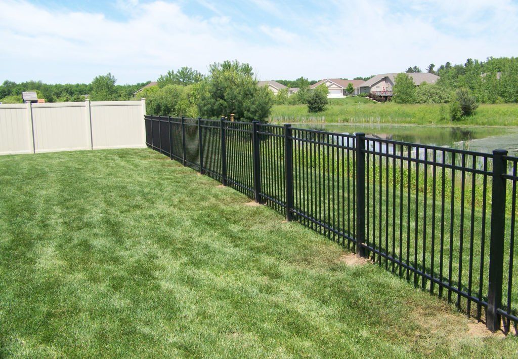 A black fence surrounds a lush green yard next to a pond.