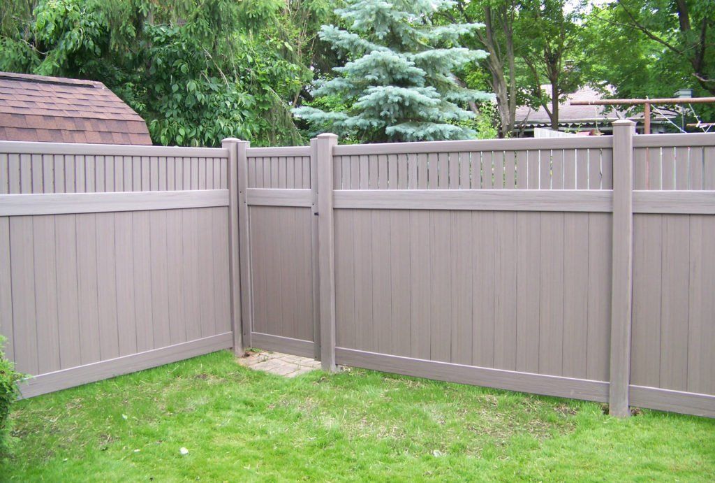 A brown vinyl fence is in the middle of a lush green yard.