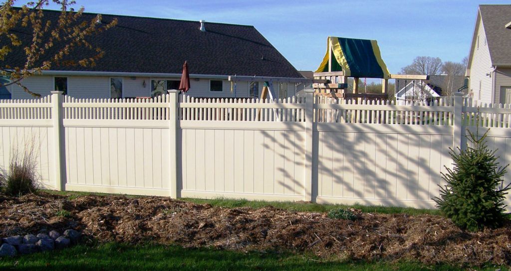 A white fence surrounds a backyard with a playground in the background.