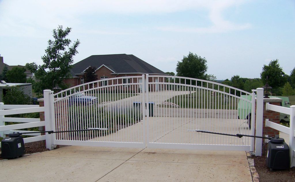 A white gate is open to a driveway in front of a house