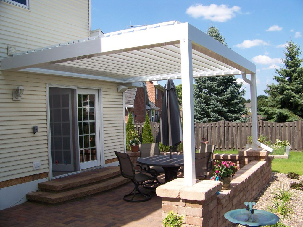 A patio with a table and chairs under a white motorized pergola