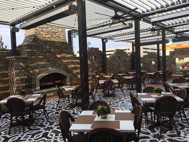 A restaurant with tables and chairs and a fireplace under a motorized pergola