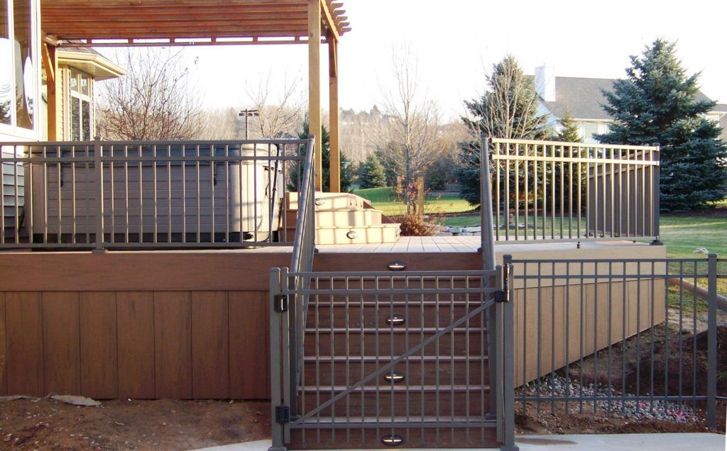 A fence leading to a deck with a hot tub underneath it