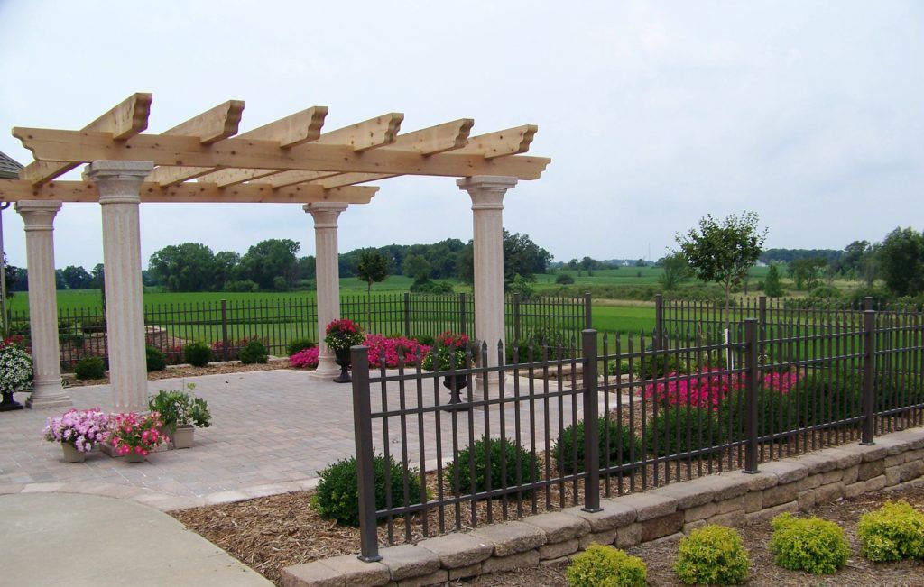 A pergola is surrounded by a fence and flowers