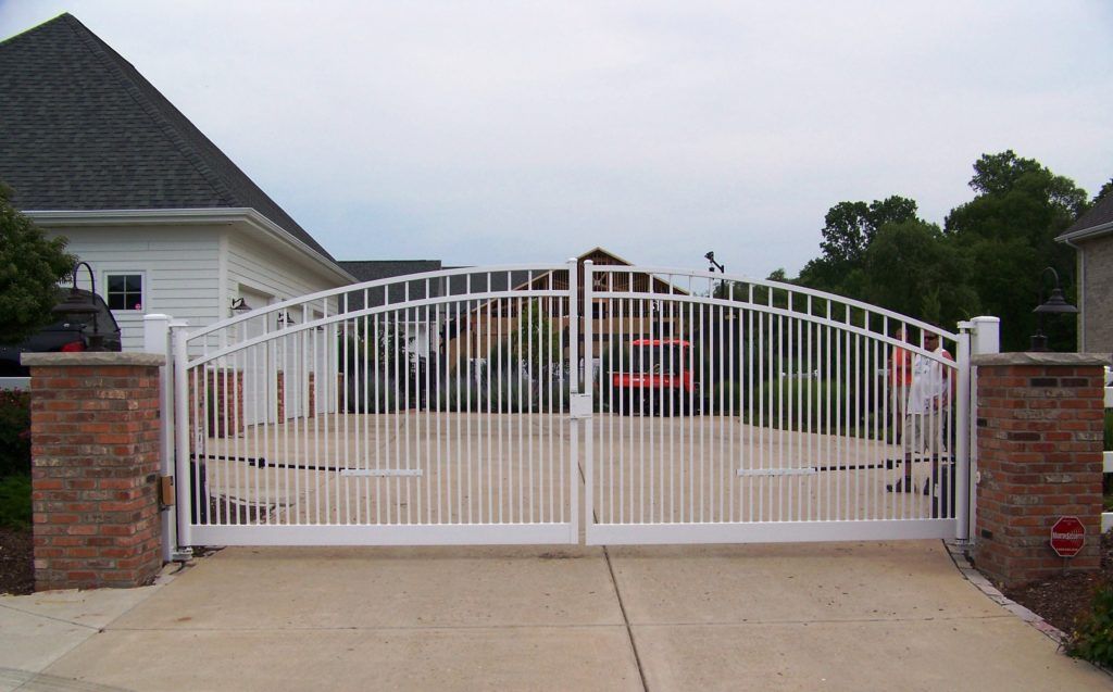 A white gate is open to a driveway in front of a house