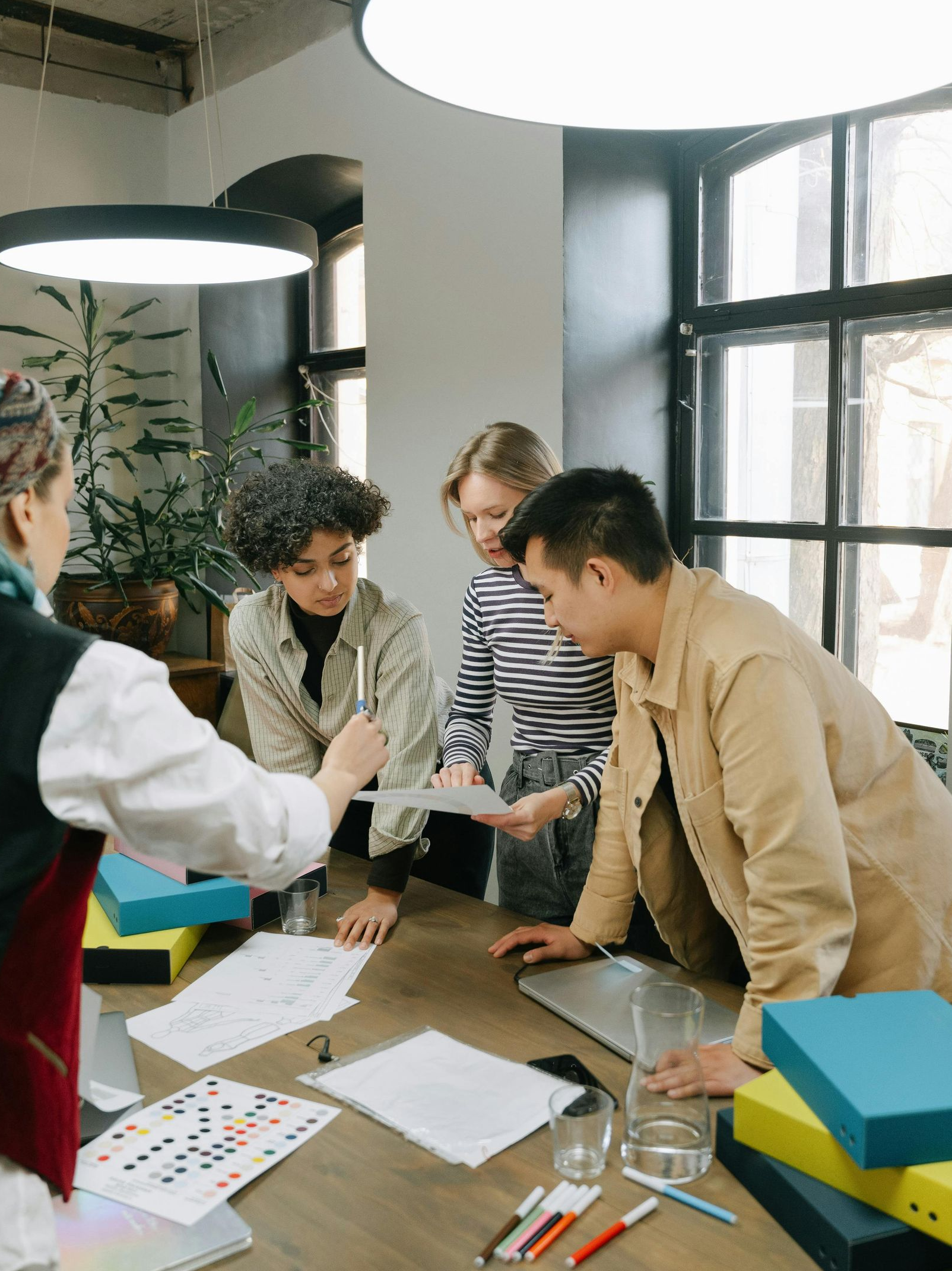 A diverse group of colleagues collaborate around a desk, reviewing documents and diagrams in a bright office space.