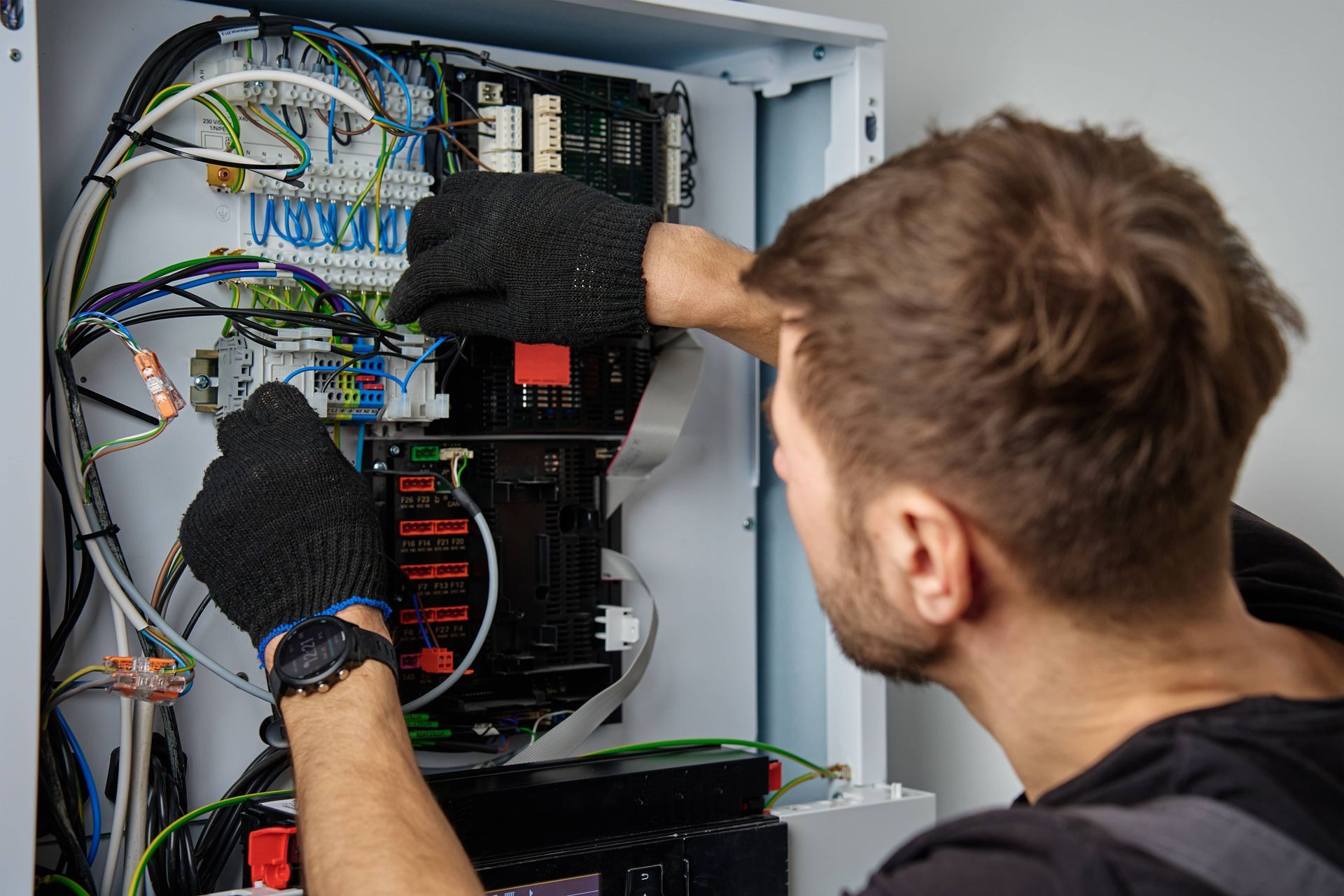 Technician in gloves works on the complex internal wiring and components of an electrical control panel.