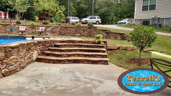 A stone wall surrounds a swimming pool with stairs leading up to it.