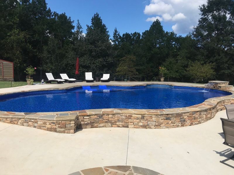 A large swimming pool surrounded by chairs and trees on a sunny day