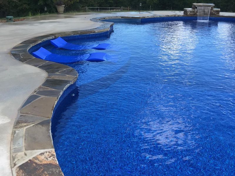 A large swimming pool with blue chairs and a waterfall.