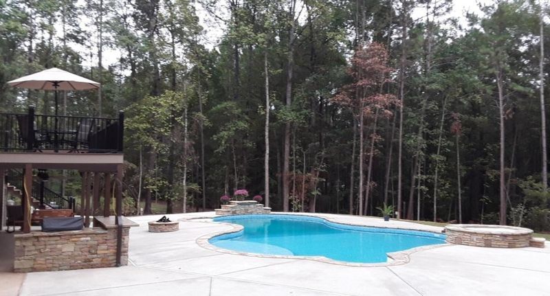 A large swimming pool is surrounded by trees and a gazebo.