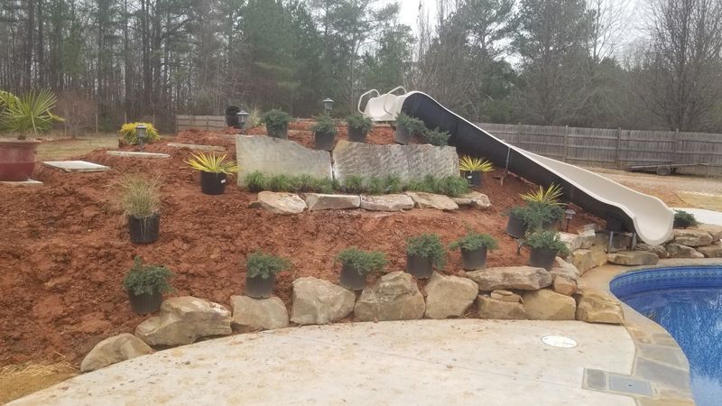 A slide is sitting on top of a rocky hill next to a pool.