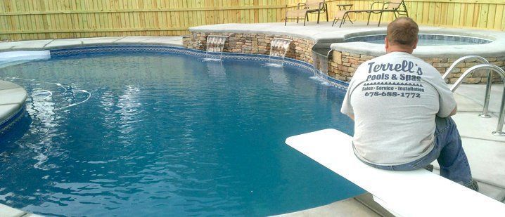 A man is sitting on a diving board in front of a swimming pool.