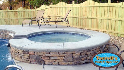A hot tub is surrounded by a stone wall next to a swimming pool.