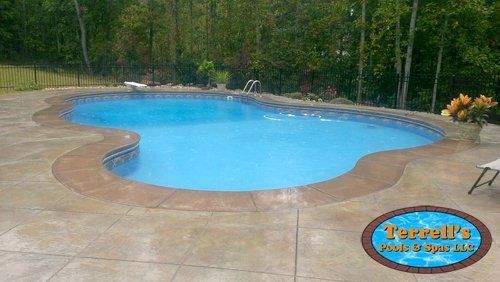 A large swimming pool is surrounded by trees and a patio.