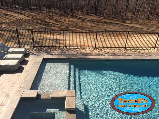 A large swimming pool is surrounded by a fence and chairs.