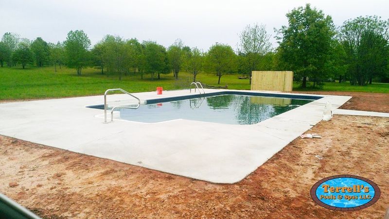 A large swimming pool is surrounded by dirt and trees.