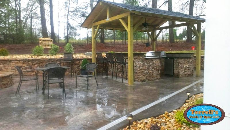 A patio with a gazebo , tables and chairs and a grill.
